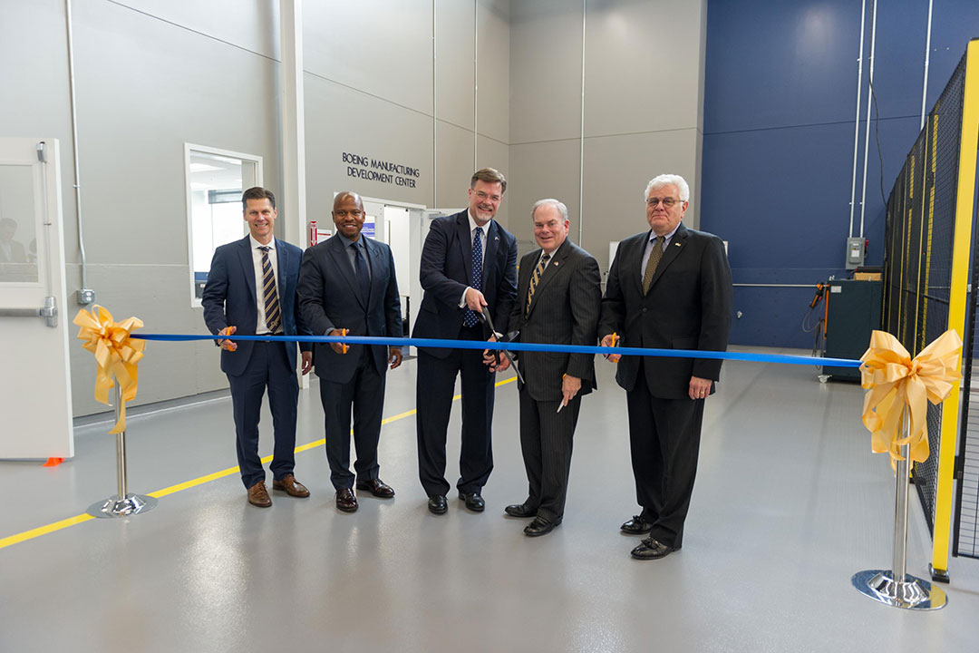 Five men about to cut a ribbon in front of a sign that says "Boeing Manufacturing Development Center"