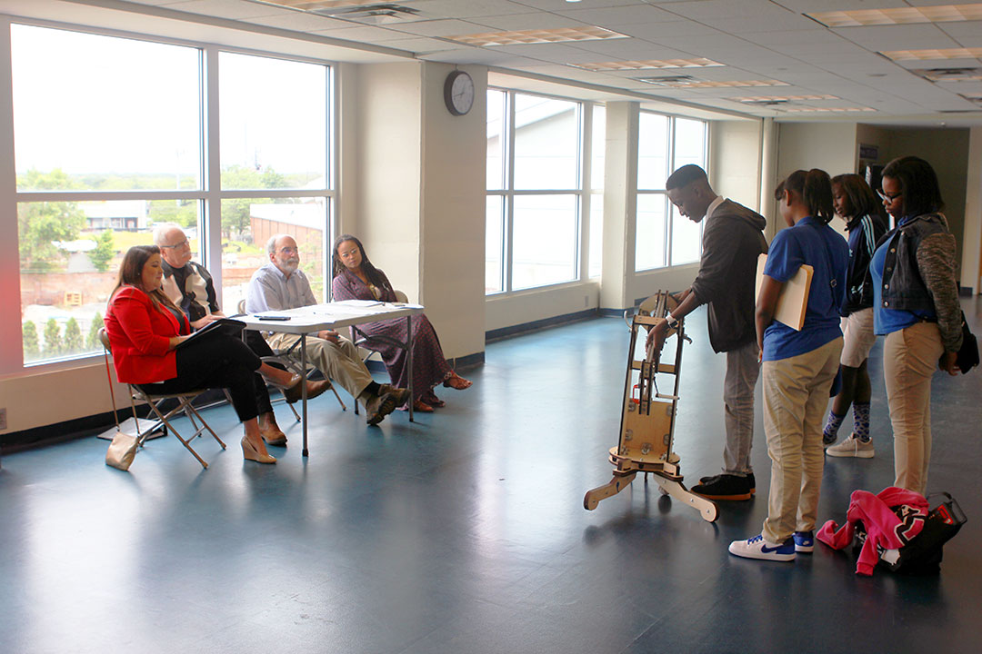 A group of students demonstrating a baseball launching invention to a panel of judges