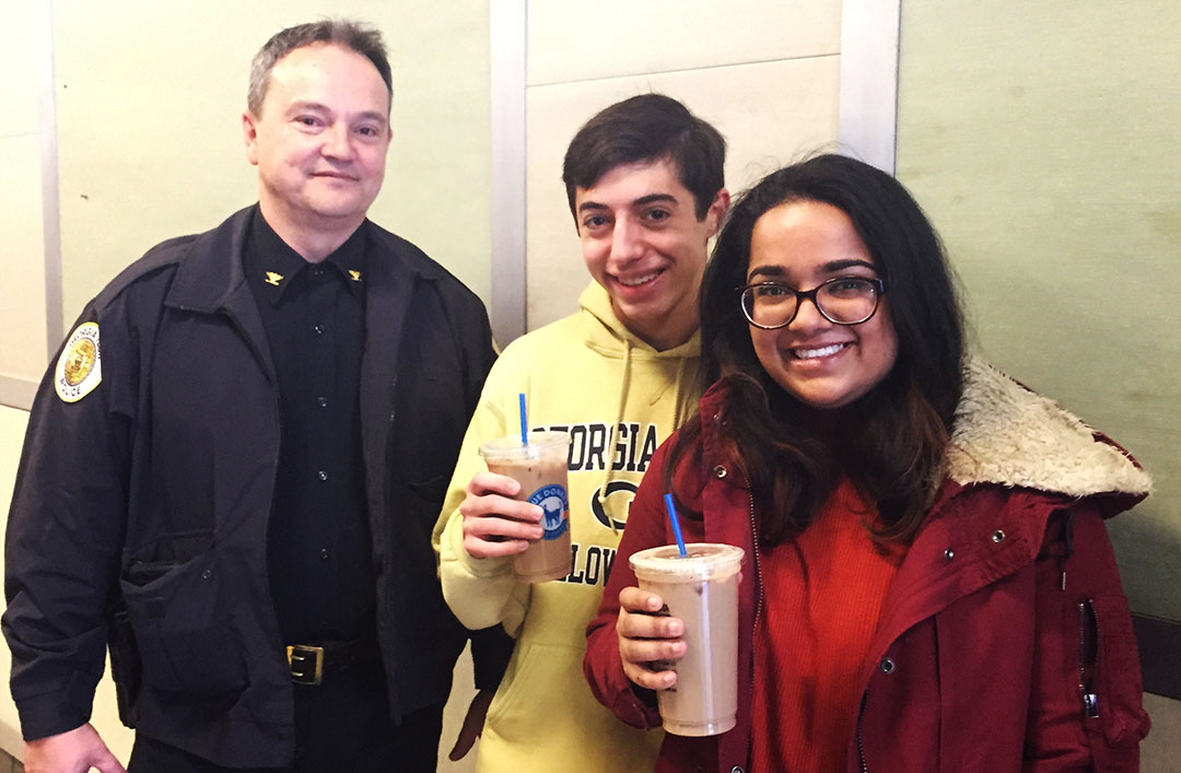 The Georgia Tech chief of police poses for a picture with two undergrads who are drinking Blue Donkey iced coffee