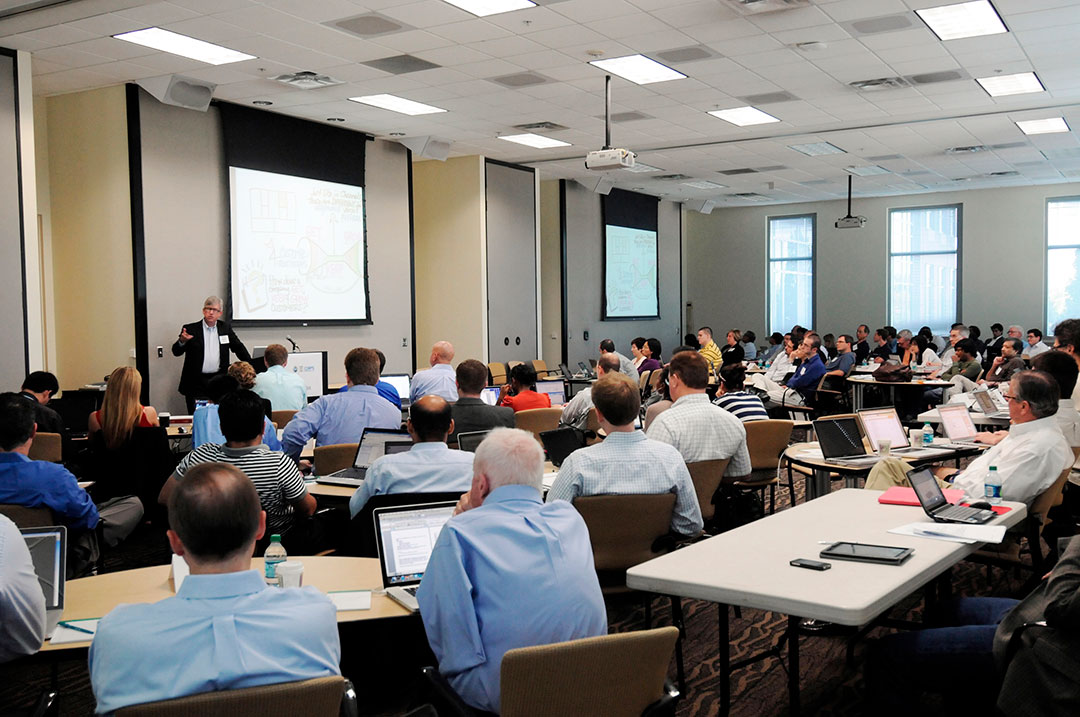 A large crowd listening to a speaker at the front of a lecture hall