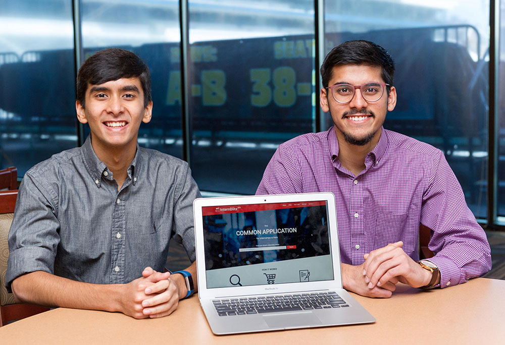 Two young, well-dressed men sit at a table in front of a computer screen showing their site, which says The common app for internships is here