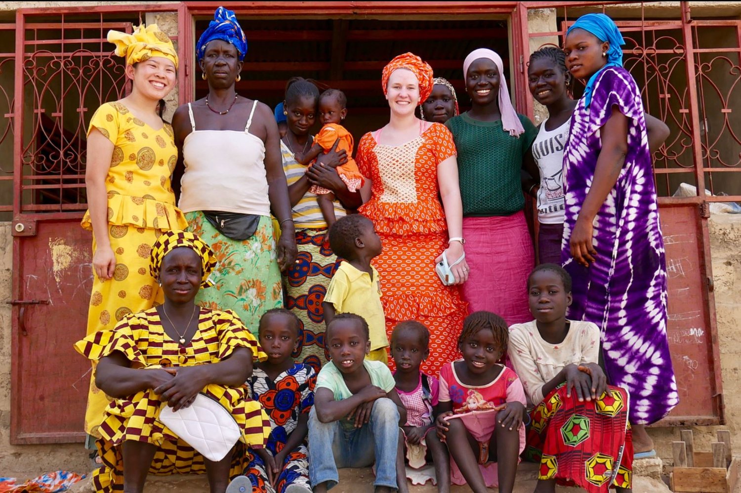 A group of students with local Senegalese people, all of whom are wearing colorful Senegalese clothing