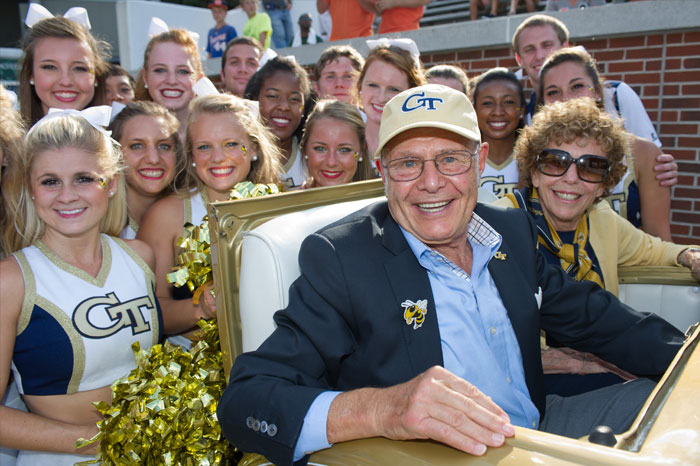 Ernest and Roberta Scheller riding in the Ramblin Wreck with cheerleaders surrounding them