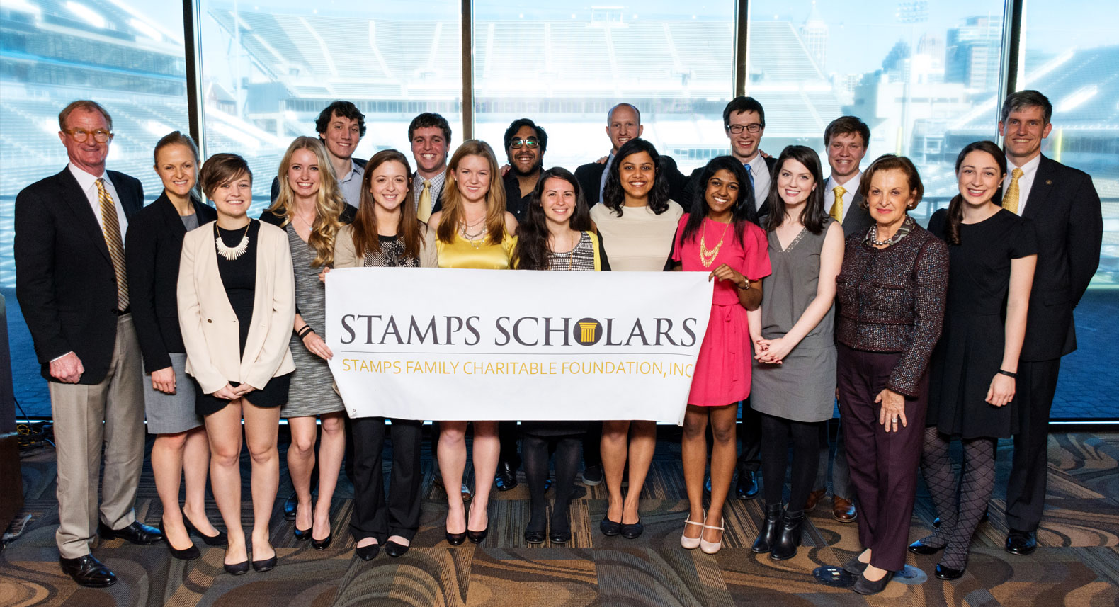 Group photo of scholars holding a banner that says "Stamps Scholars" with E. Roe and Peggy Stamps