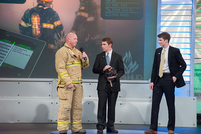 Zack Braun and Tyler Sisk on stage with a firefighter during the Inventure Prize competition